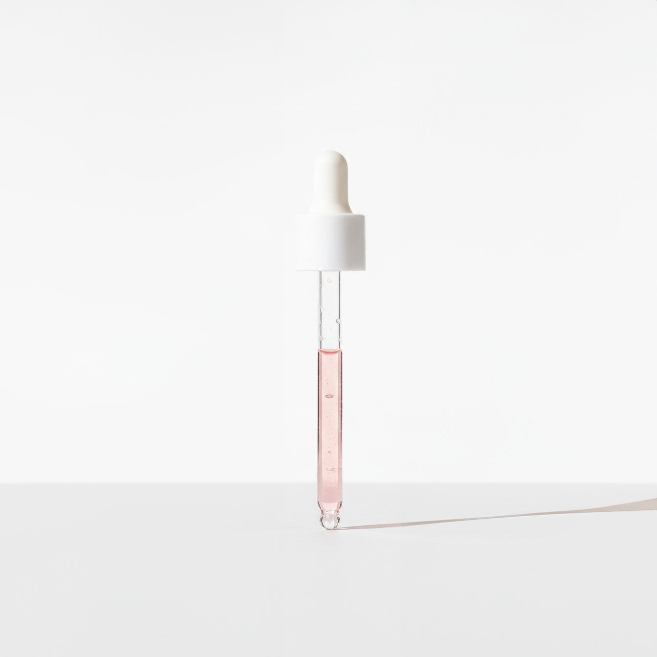 White dropper with a clear pink liquid on a white background