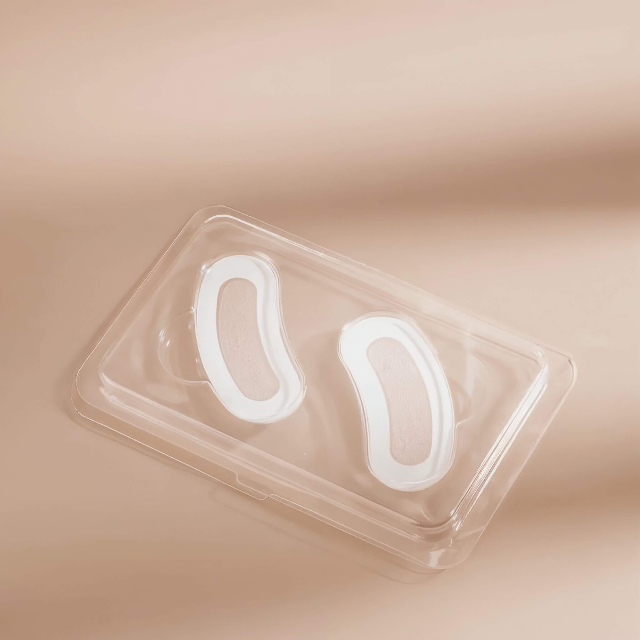 Two transparent Skintual under eye patches in a clear plastic case on a beige background