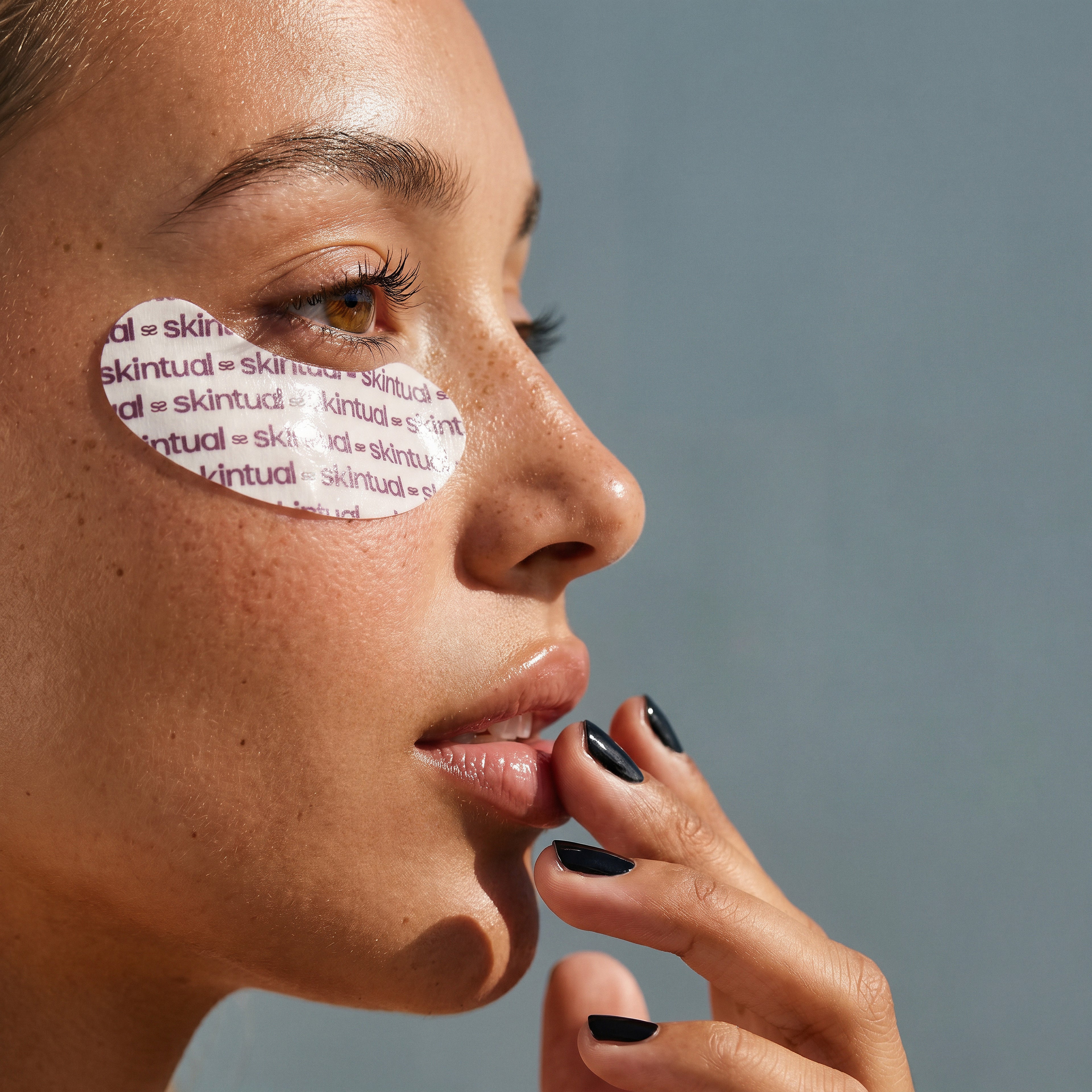 Close-up of a woman's face with a Skintual patch on her eye against a gray background